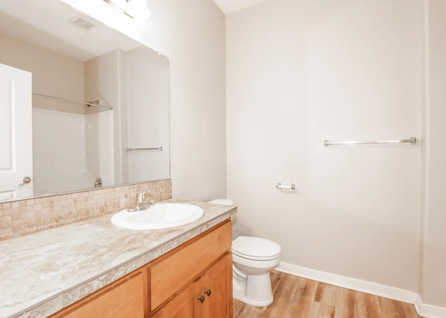 Bathroom in an apartment featuring a marble countertop sink, a toilet, wooden cabinets, and a large mirror with a towel rack on the wall.