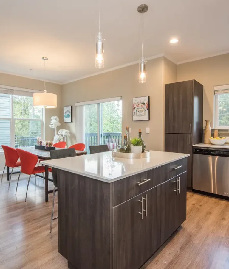 Modern apartment interior featuring an open-plan kitchen and dining area with wooden flooring, dark cabinetry, an island, and large windows providing natural light.
