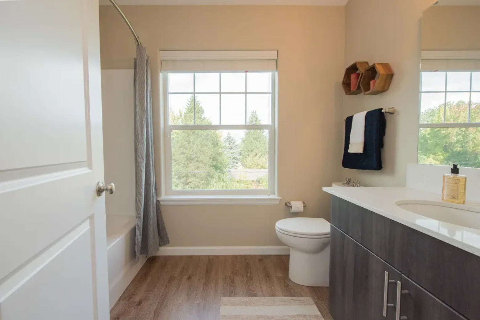 Bathroom in an apartment featuring a bathtub with a curtain, a window with a view of trees, and a modern sink with a dark cabinet.