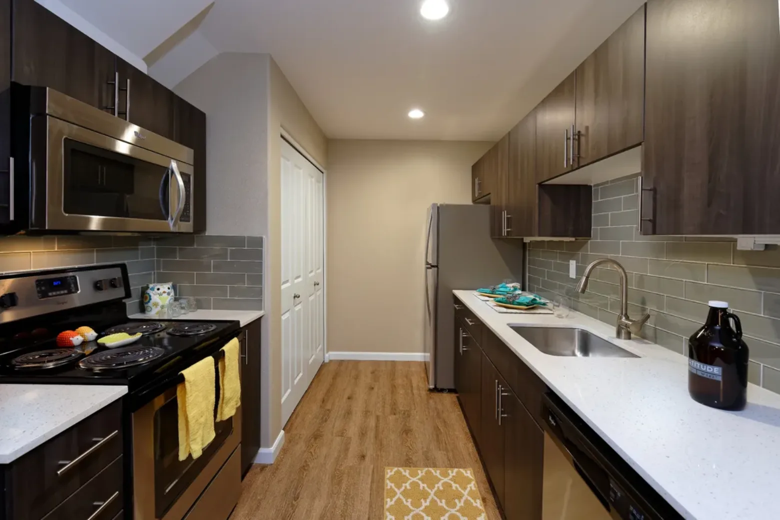 Modern kitchen in an apartment featuring dark wood cabinets, stainless steel appliances, white countertops, and a gray subway tile backsplash.