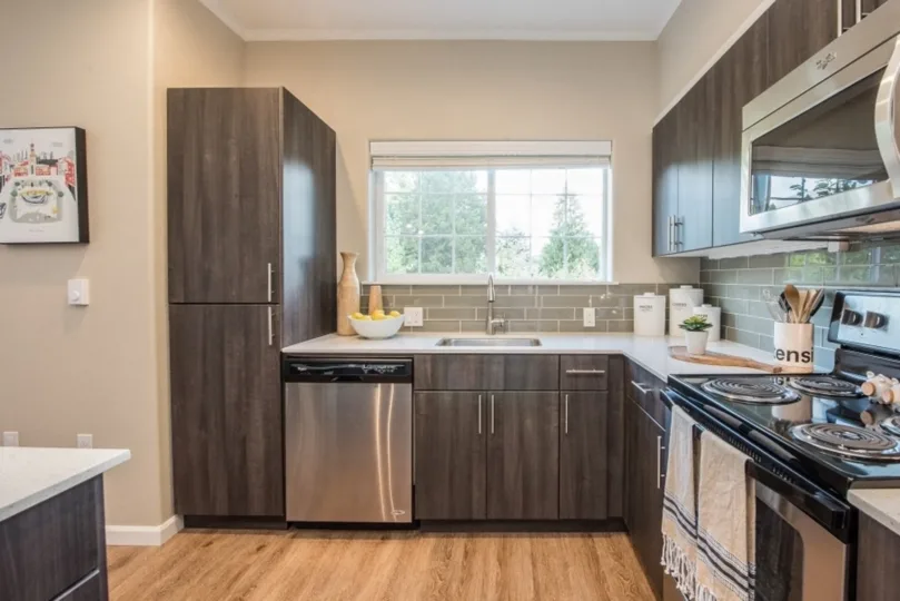 Modern kitchen featuring dark wood cabinets, a stainless steel stove and microwave, a sink under a large window, and decorative items on the countertop.